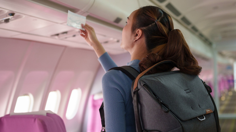 A woman with a backpack holding up her ticket to the aisle numbers to compare