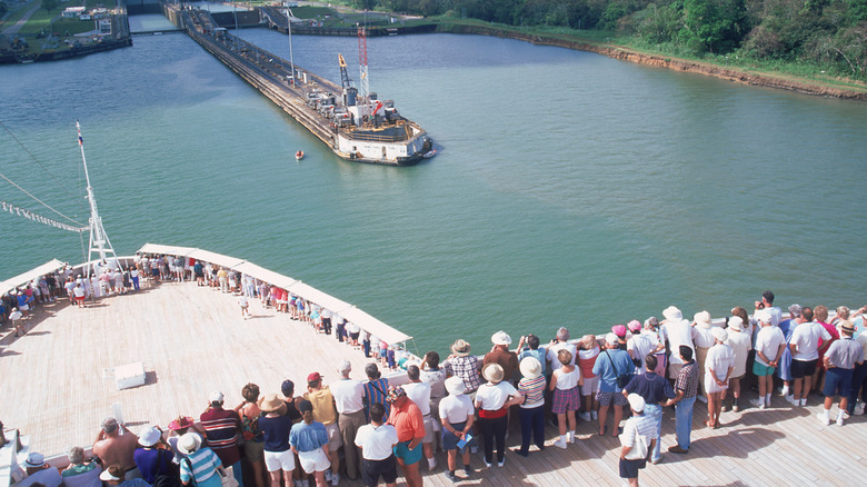 Passengers crowd the deck of a cruise liner going through a canal