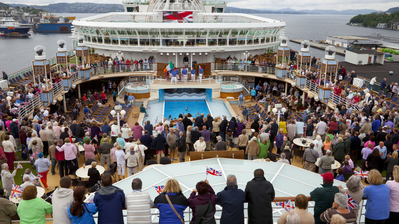 Hundreds of people gather around a swimming pool on the deck of a cruise ship