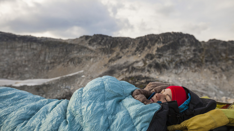 A woman sleeping in a sleeping bag outdoors in the mountains