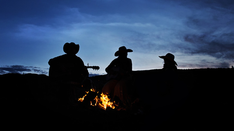 A group of cowboys gathering under a fire in the desert