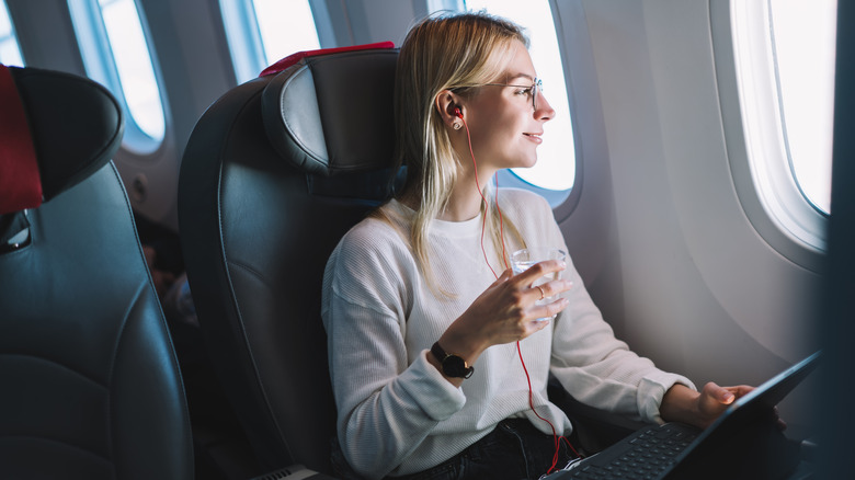 Woman holding a drink and looking out the window on a plane