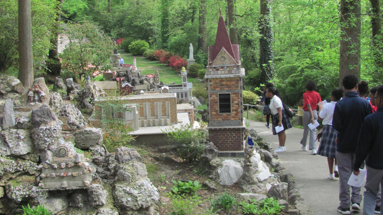 One of the statues in a grotto in Ave Maria Grotto with people walking on a path nearby