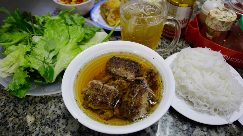 Pork patties in soup with a plate of lettuce and ride noodles with drink