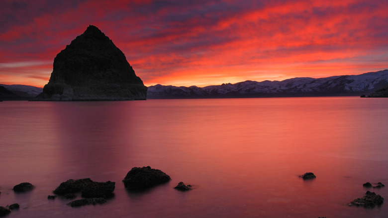 pyramid shaped rock silhouetted against the sunset on a lake