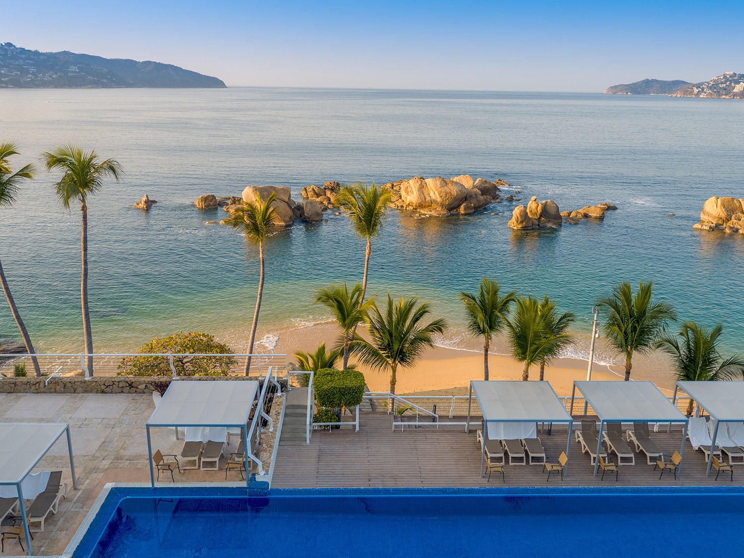 A beach resort pool and lounge with a view of the ocean.