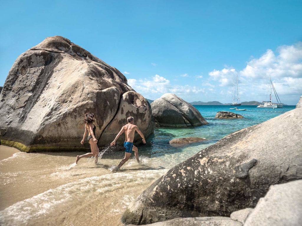 A couple running through rocky areas on a beach side.